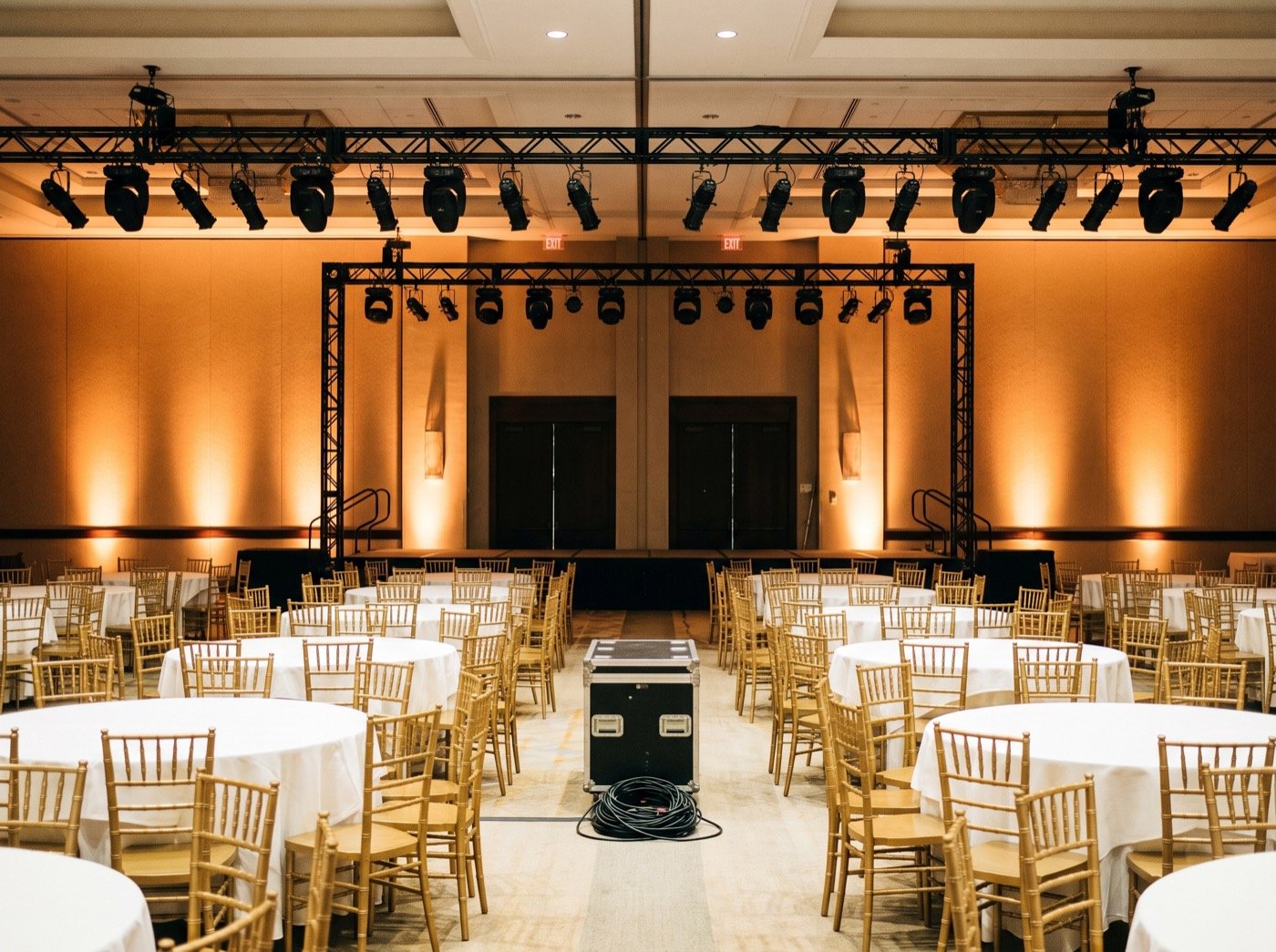 Empty ballroom with gold chairs, white tables and stage rigging