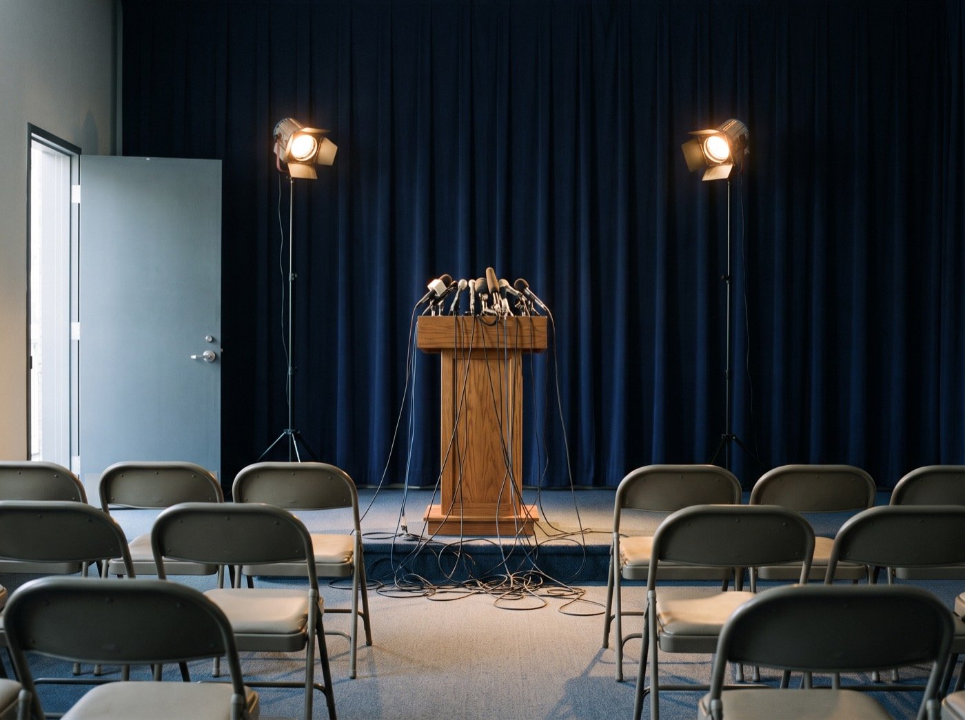 Podium with a cluster of microphones facing rows of empty chairs