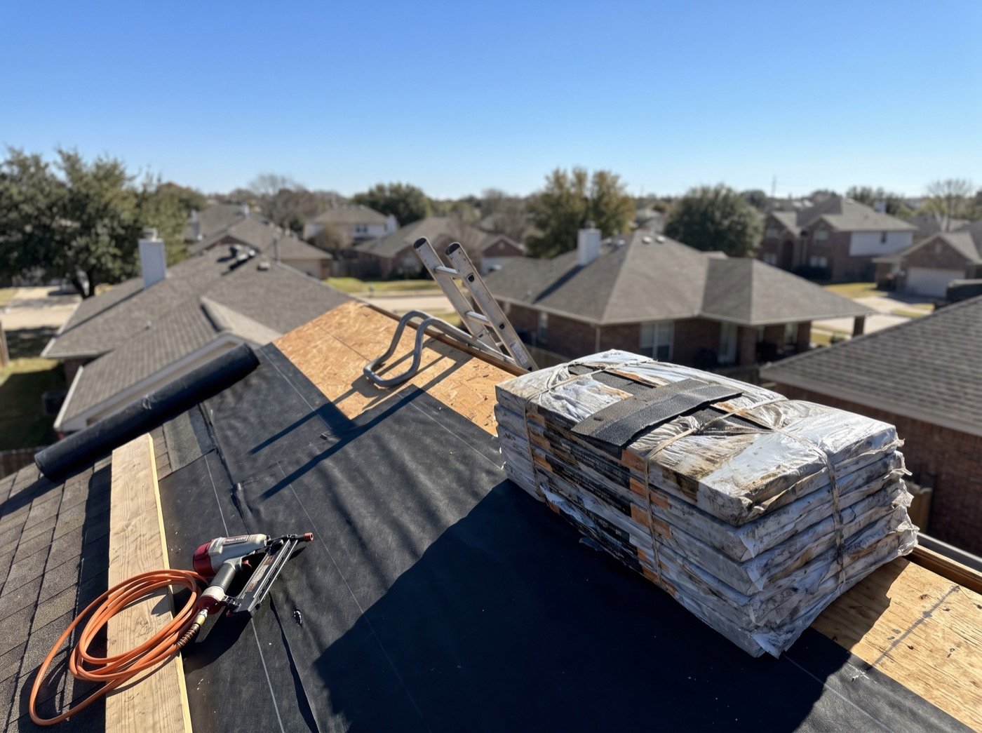 Stacked shingle bundles and a nail gun on a pitched roof