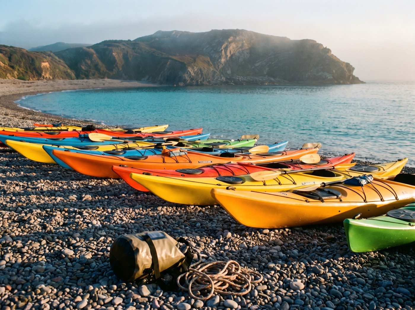 Colourful kayaks lined up on a pebble beach at sunrise